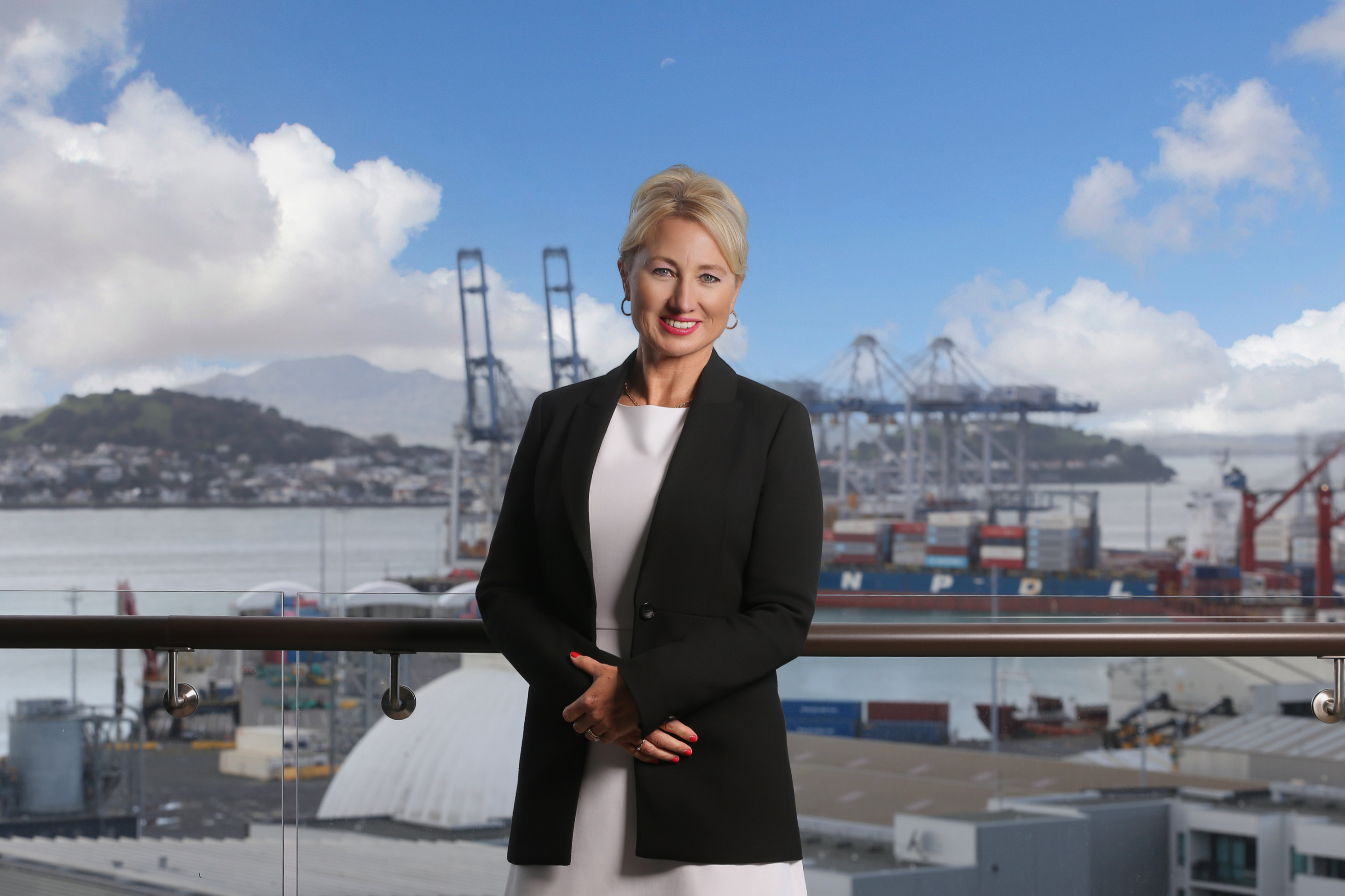 Genevieve Sage in a black jacket, smiling with a city and port background